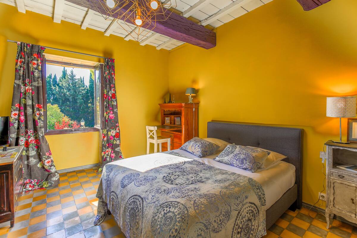 A bedroom with a bed, a desk, and a window with curtains.