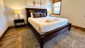 A bedroom with a wooden bed, two bedside tables with lamps, a patterned rug, and a window with blinds. - Pet-Friendly Driggs Condo Near Targhee (Driggs)