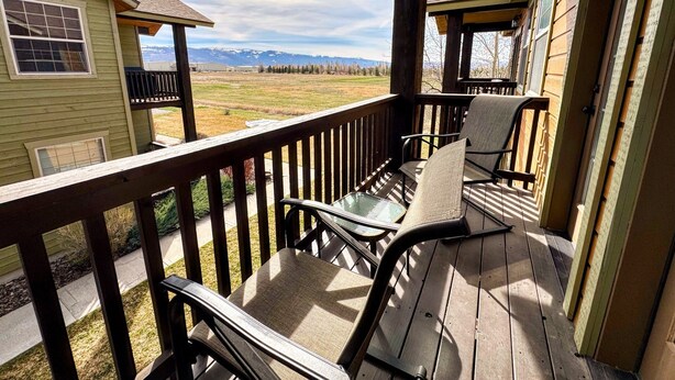 A wooden deck with chairs and a table, overlooking a grassy field and mountains. - Pet-Friendly Driggs Condo Near Targhee (Driggs)