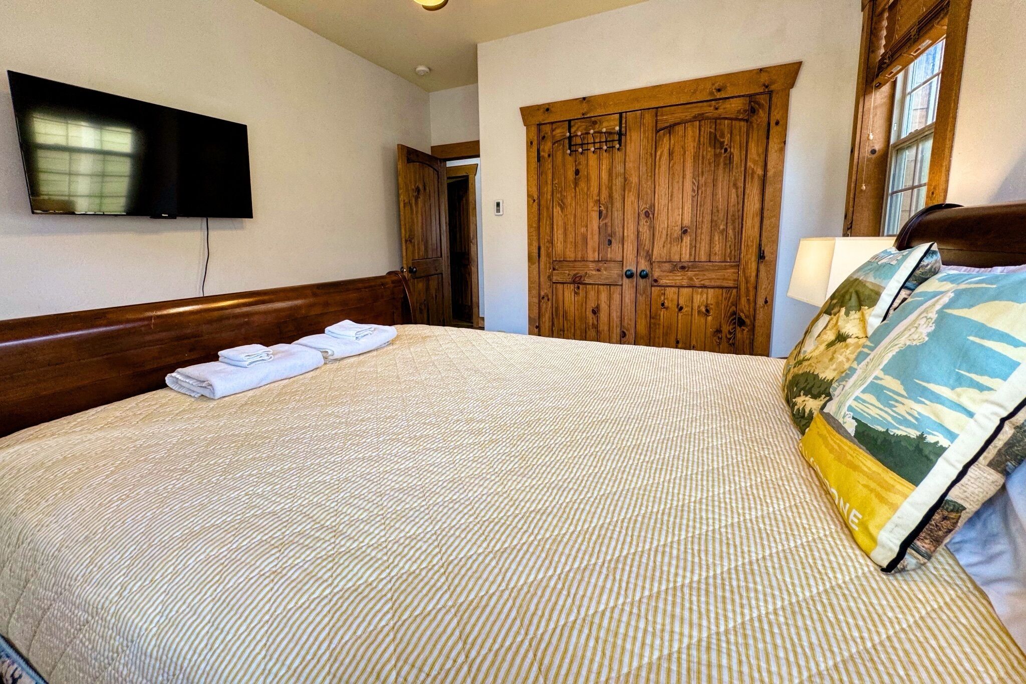 Ein Hotelzimmer mit einem großen Bett, einem flachbildfernseher an der Wand, einem Holzschrank und einem Fenster.