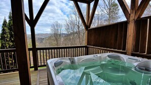 A hot tub on a wooden deck with a view of trees and hills. - Experience luxury in this 6-bedroom cabin in Sugar Grove, NC, ideal for 12! (Sugar Grove)