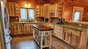 A log cabin kitchen with wooden cabinets, a central island, and a refrigerator. - Experience luxury in this 6-bedroom cabin in Sugar Grove, NC, ideal for 12! (Sugar Grove)