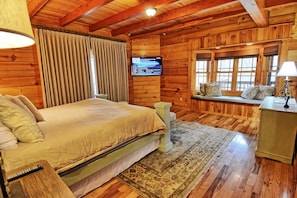 Une chambre dans un chalet en bois, avec un lit, une télévision, un banc avec des coussins et un bureau avec une lampe.