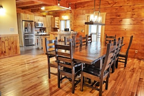 Un intérieur en bois avec une table à manger entourée de chaises, un coin cuisine équipé d’appareils électroménagers et une fenêtre laissant entrer la lumière naturelle.