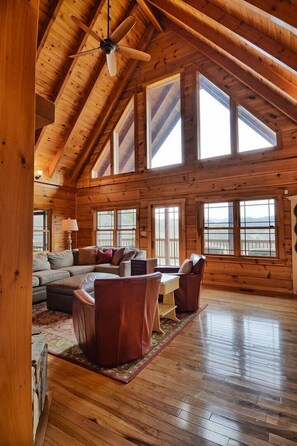 A spacious wooden cabin with a high ceiling, large windows, and a cozy seating area.