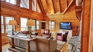 A cozy cabin interior with wooden walls, a stone fireplace, a television, and a comfortable seating area. - Experience luxury in this 6-bedroom cabin in Sugar Grove, NC, ideal for 12! (Sugar Grove)