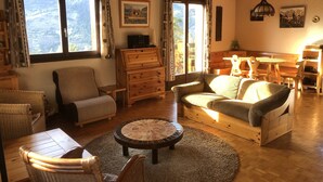 A cozy living room with a wooden sofa, a round coffee table, and a dining area with wooden furniture. - Spacious, 6-person chalet with stunning views in La Norma, French Alps (La Norma)