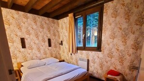 A bedroom with a wooden ceiling, a bed, a window with curtains, and a small stool. - Spacious, 6-person chalet with stunning views in La Norma, French Alps (La Norma)