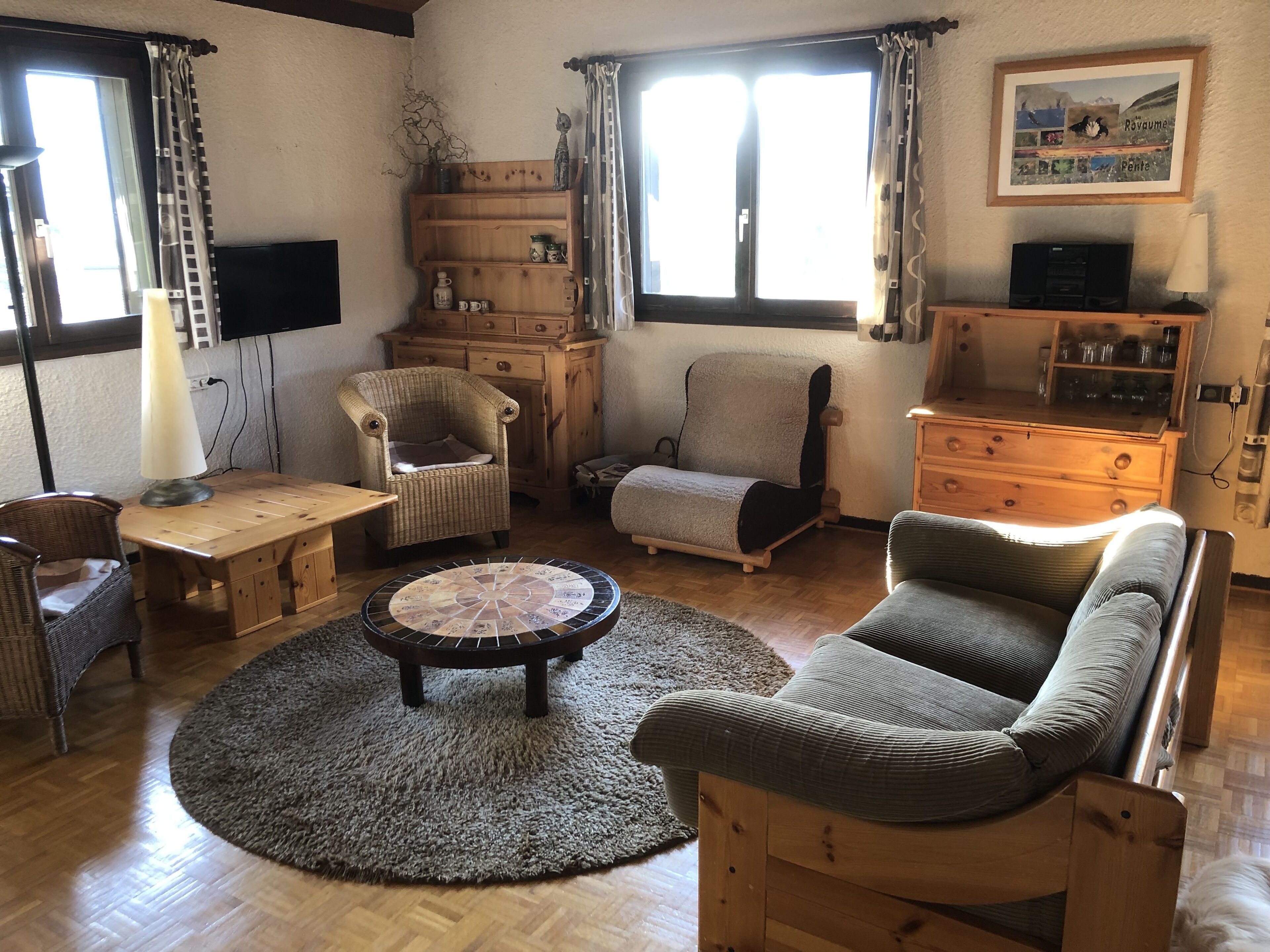 Un salon chaleureux avec une table basse en bois, deux fauteuils, un canapé et un téléviseur posé sur un meuble en bois.