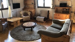 A cozy living room with a wooden coffee table, two armchairs, a sofa, and a TV on a wooden stand. - Spacious, 6-person chalet with stunning views in La Norma, French Alps (La Norma)