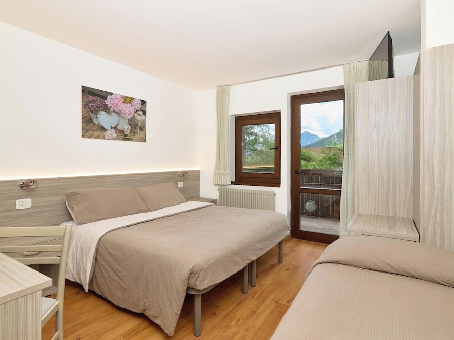 Quarto com cama, mesa de cabeceira e janela com vista para vegetação e montanhas.