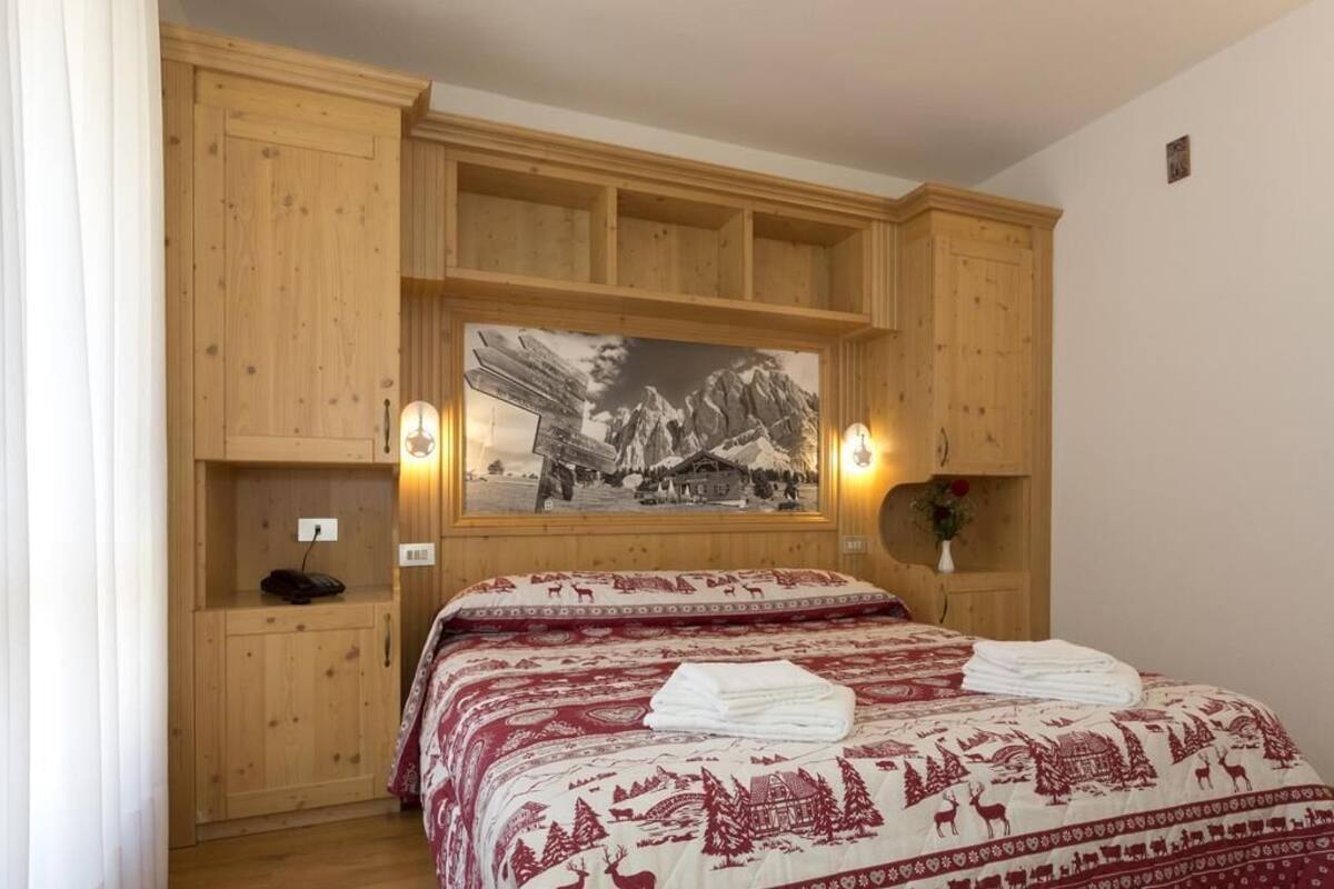 Een slaapkamer met een houten garderobe, een bed met een bedovertrek met patroon en een lijst met een afbeelding erboven.