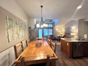 A dining area with a wooden table and chairs, a stone fireplace, and a view of the outdoors.