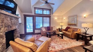 A spacious living room with a stone fireplace, leather sofas, a coffee table, and a ceiling fan. - Mountain Thunder Townhome • Ski-In • Pools Hot Tubs • Walk to Main St (Breckenridge)
