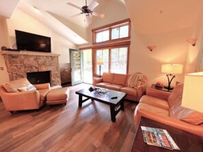 A living room with a fireplace, a television, and a ceiling fan.