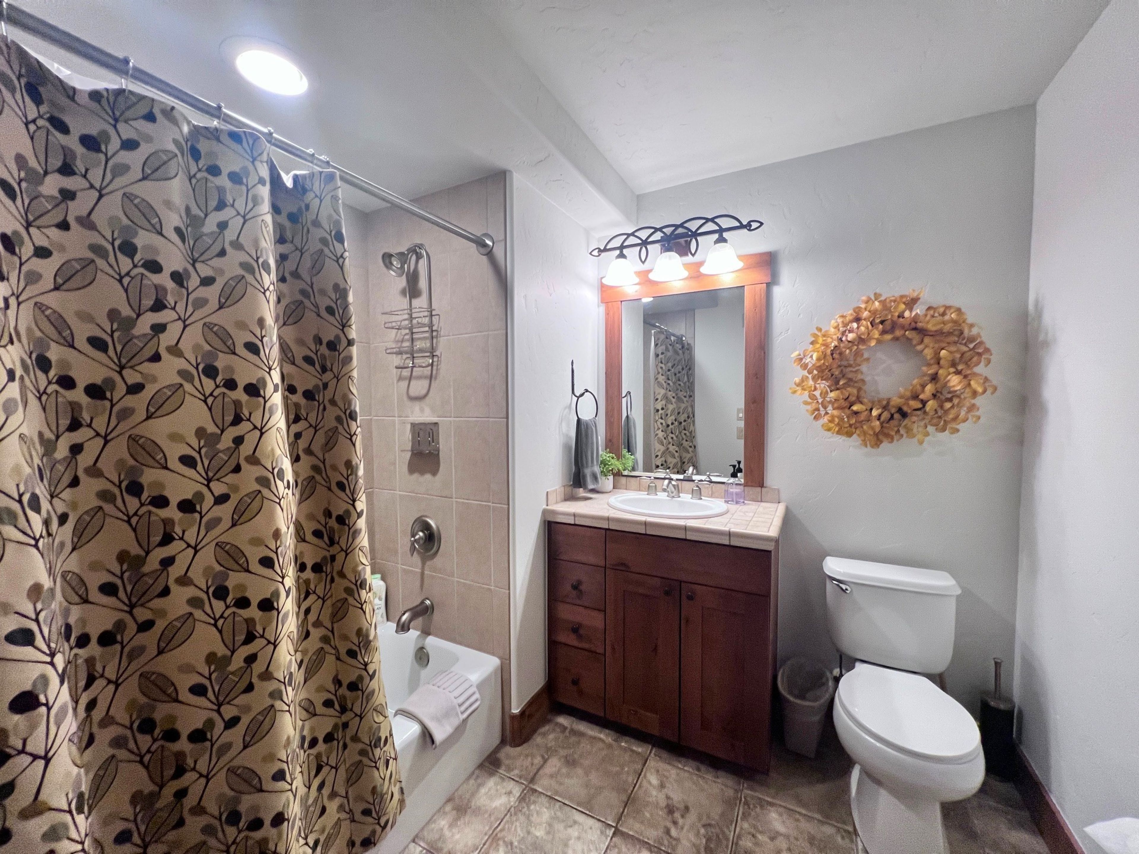 A bathroom with a shower curtain, a bathtub, a sink with a mirror, and a toilet.