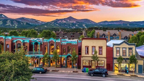 A street view of a town with historic buildings, a clear sky, and mountains in the background. - Mountain Thunder Townhome • Ski-In • Pools Hot Tubs • Walk to Main St (Breckenridge)