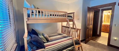 Una cama litera con escalera, una ventana con persianas y una puerta que da a un baño.