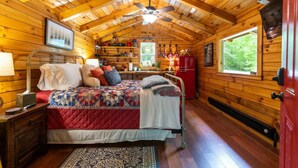Un dormitorio de cabaña acogedor, con una cama, una mesita de noche, un aparador, un refrigerador rojo y una ventana con vista a follaje verde.