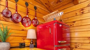 Una cocina compacta con un refrigerador rojo, paredes de madera, una mesita y ollas colgantes.