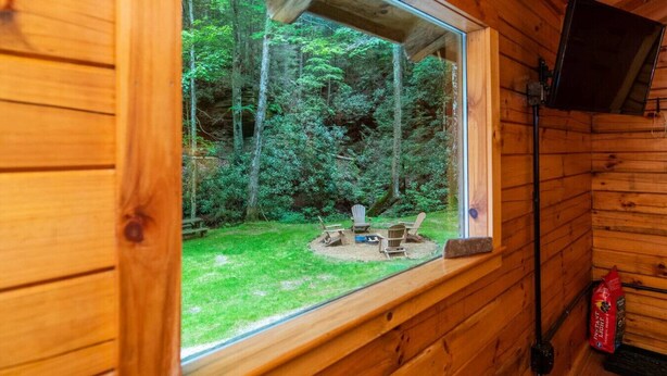 Una cabaña de madera con un ventanal grande que da a una zona boscosa. En el interior, hay un banco de madera y una pequeña mesa con sillas.
