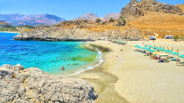 A beach with clear turquoise waters, rocky cliffs, and a sandy shore with umbrellas and beach chairs. - Villa Evelina | Private Pool (Adelianos Kampos)