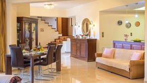 A spacious living area with a dining table set for four, a sofa, and a staircase leading to an upper level. - Villa Evelina | Private Pool (Adelianos Kampos)