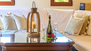 A glass-top table with a candle, wine bottle, and glasses, set on a white sofa with patterned pillows. - Villa Evelina | Private Pool (Adelianos Kampos)