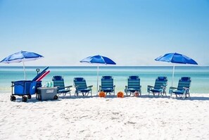 En strand med blå parasoller og badestole i rækker.
