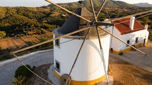 A windmill with a white and yellow base, a black roof, and a wooden structure with ropes. - Charming windmill between nature and sea (Palmela)