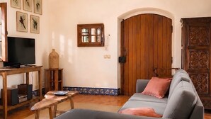 A living room with a sofa, television, wooden cabinet, and a door with an arch. - Charming windmill between nature and sea (Palmela)