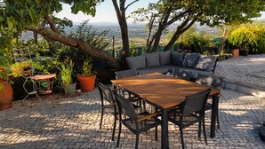 A patio with a wooden table and chairs, a gray sofa, and potted plants. - Charming windmill between nature and sea (Palmela)