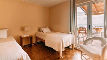 Une chambre d’hôtel avec deux lits, une petite table avec une lampe, une chaise et un balcon avec vue sur la mer.