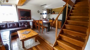 Ett mysigt vardagsrum med en soffa i läder, ett soffbord i trä och en trappa som leder upp till ett köksområde.