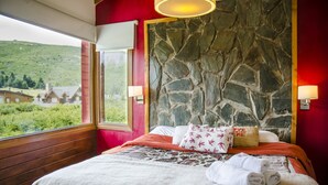 Ett hotellrum med en sänggavel i sten, en säng med ett mönstrat överkast och utsikt över ett grönskande landskap genom ett fönster.