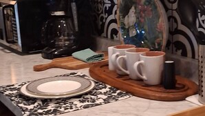 Een aanrecht met een koffiezetapparaat, mokken en een decoratief bord.