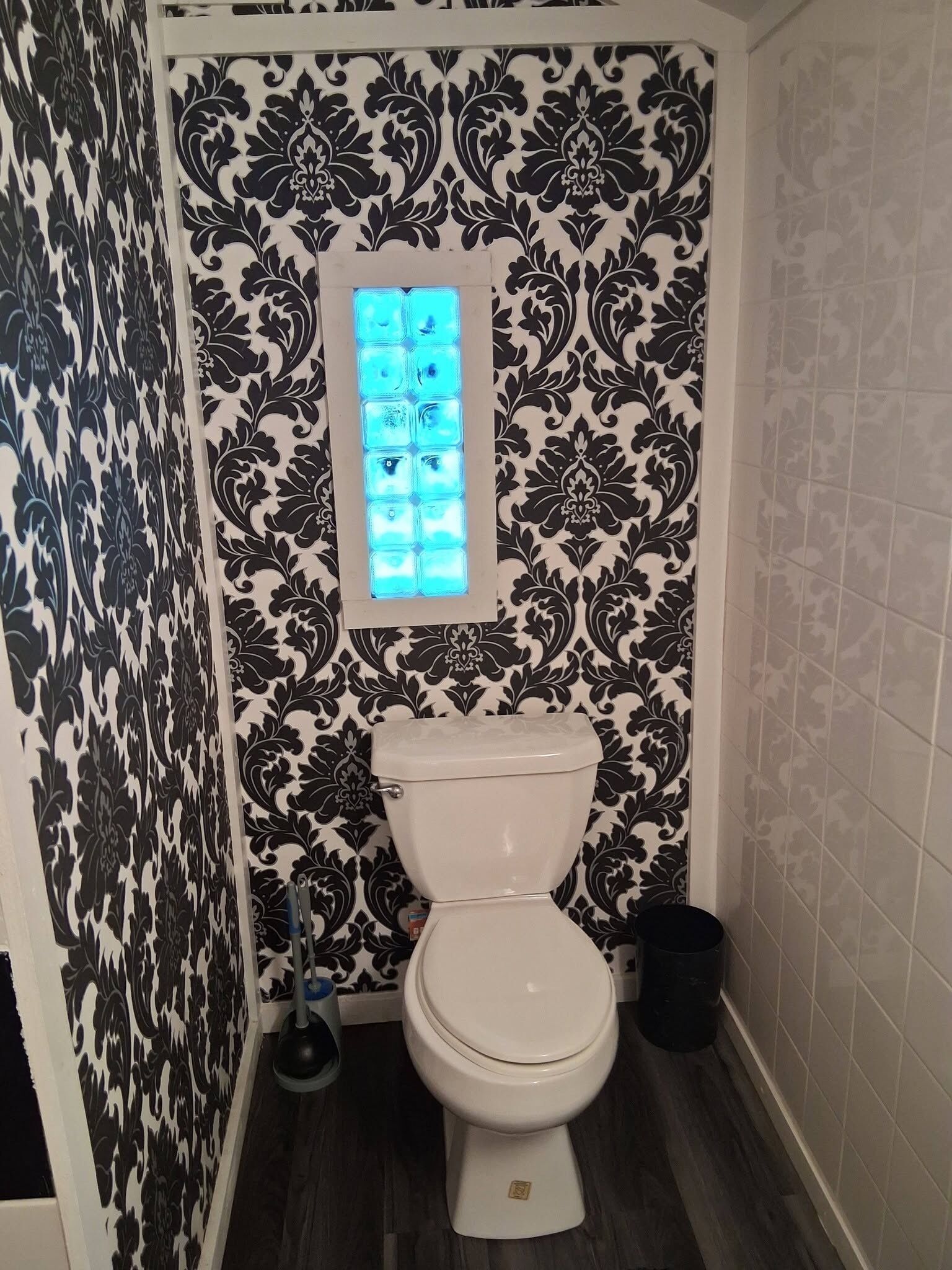Une salle de bain avec des toilettes, un panneau lumineux bleu et un papier peint à motifs.
