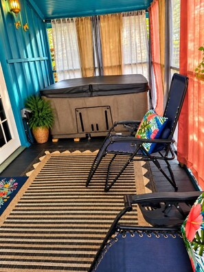 A covered patio area with a black exercise bike, a blue lounge chair with a floral cushion, and a patterned rug. - RELAX! UNPLUG, SOAK IN THE HOT TUB, VISIT RATCLIFF LAKE, STAR GAZING (Kennard)