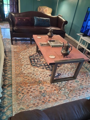 A living room with a brown leather sofa, a coffee table, and a patterned rug. - MONTHLY RENTAL, KING BED, HOT TUB, WIFI, KITCHEN, KENNARD TX. 159 HWY 7 #201 (Kennard)