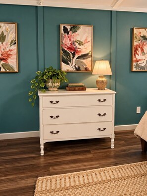 A room with teal walls, a white dresser with floral handles, a potted plant, and framed floral artwork. - RELAX! UNPLUG, SOAK IN THE HOT TUB, VISIT RATCLIFF LAKE, STAR GAZING (Kennard)
