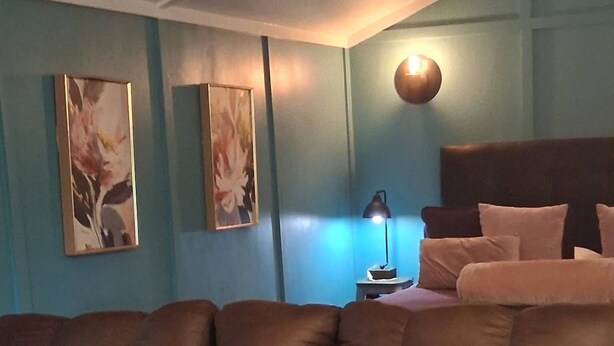 Een woonkamer met een bruine modulaire bank, een bijzettafeltje met een lamp, en twee aan de muur hangende schilderijen.