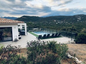 Una villa moderna con piscina, mobiliario de exterior y una vista panorámica de las colinas.