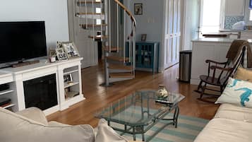 A living room with a sofa, a glass coffee table, a TV, and a staircase.