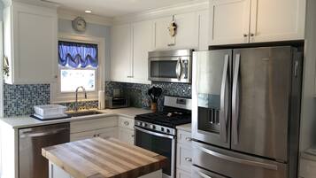 A modern kitchen with white cabinetry, stainless steel appliances, a wooden countertop, and a window with blue curtains.