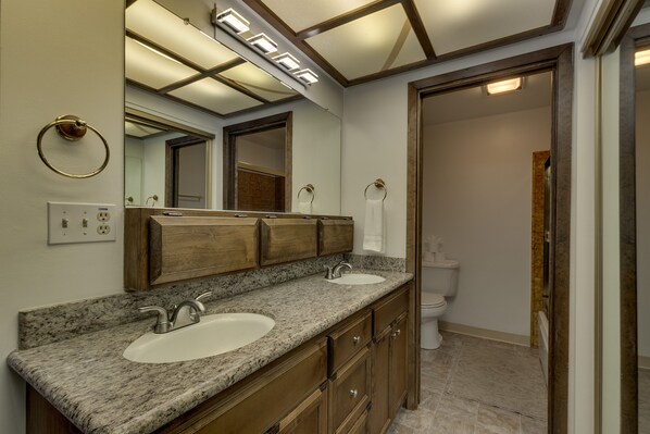 A bathroom with two sinks, wooden cabinets, a large mirror, and a toilet.