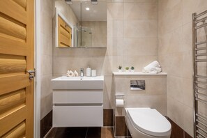 A modern bathroom with a wooden door, a white sink, a mirror, a toilet, and a towel rack. - Chic Fitzrovia 1BR by Bloomsbury (London)