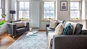 A modern living room with two sofas, a glass coffee table, and large windows offering city views.
