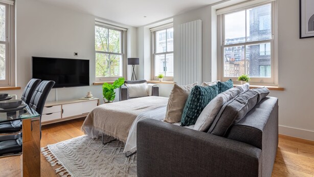 A modern bedroom with a large bed, a TV, a desk, and a window with a city view.