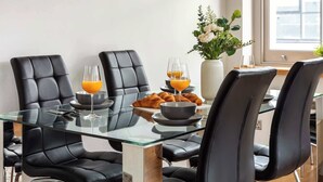 A modern dining area with a glass table, black leather chairs, breakfast items, and a vase of flowers.