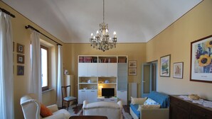 Una sala de estar con candelabro, un sofá, un sillón, un televisor y una estantería.